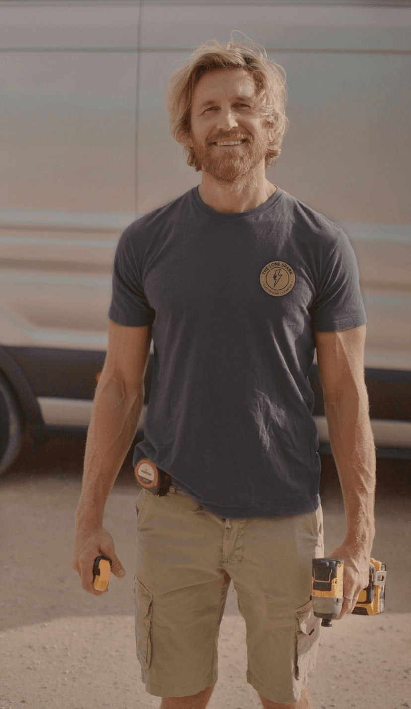 The Lone Spark electrician standing in front of van with tool belt